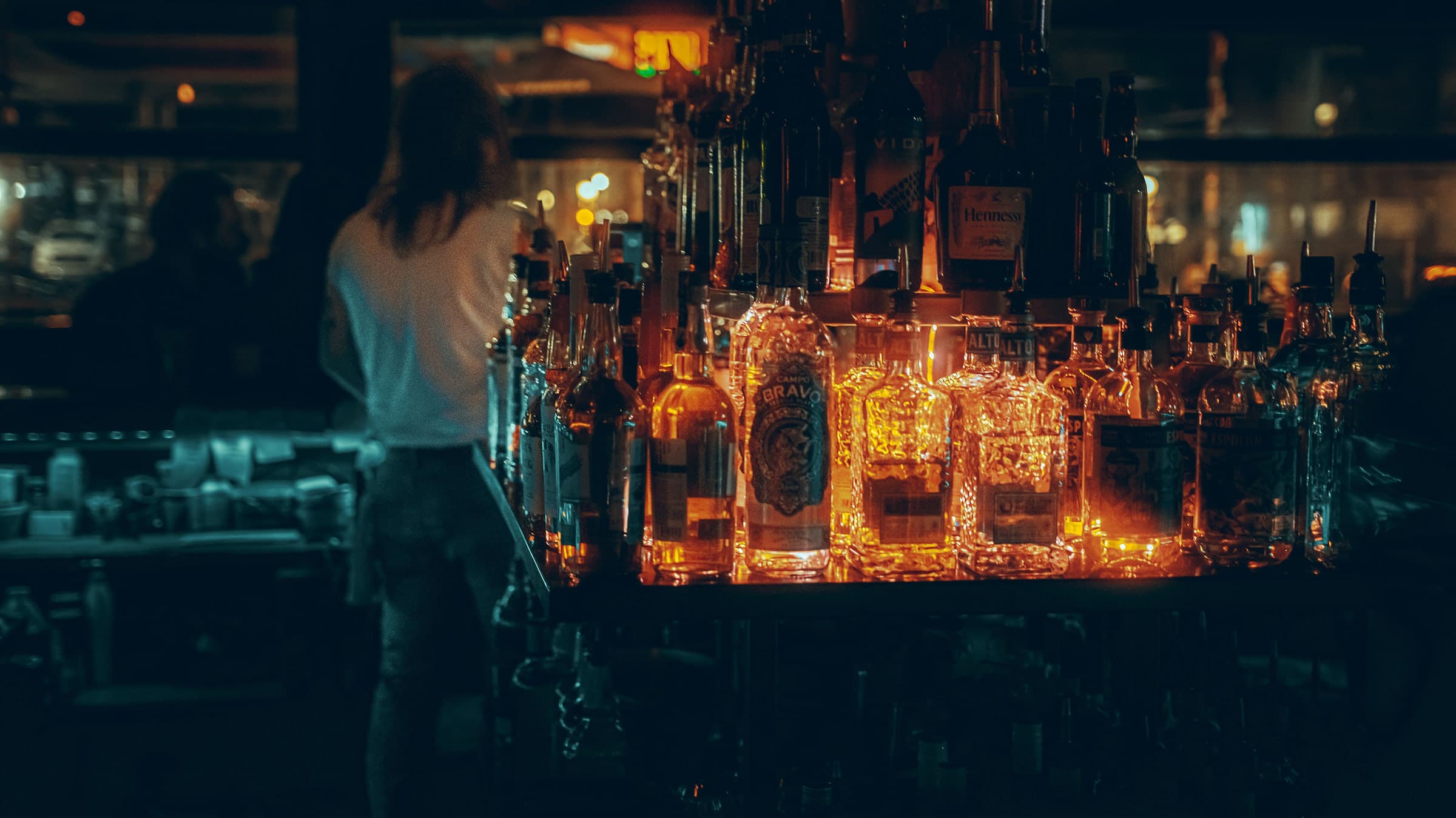 Moody cocktail bar with glowing bottles and a cocktail on the counter