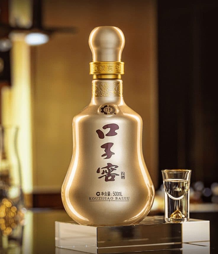 A gold Kouzijiao baijiu bottle beside a tasting glass